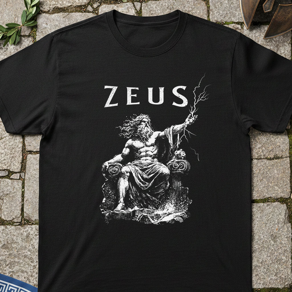 Black t-shirt with a graphic of Zeus and the word 'ZEUS' printed on it, laid flat on a stone surface.