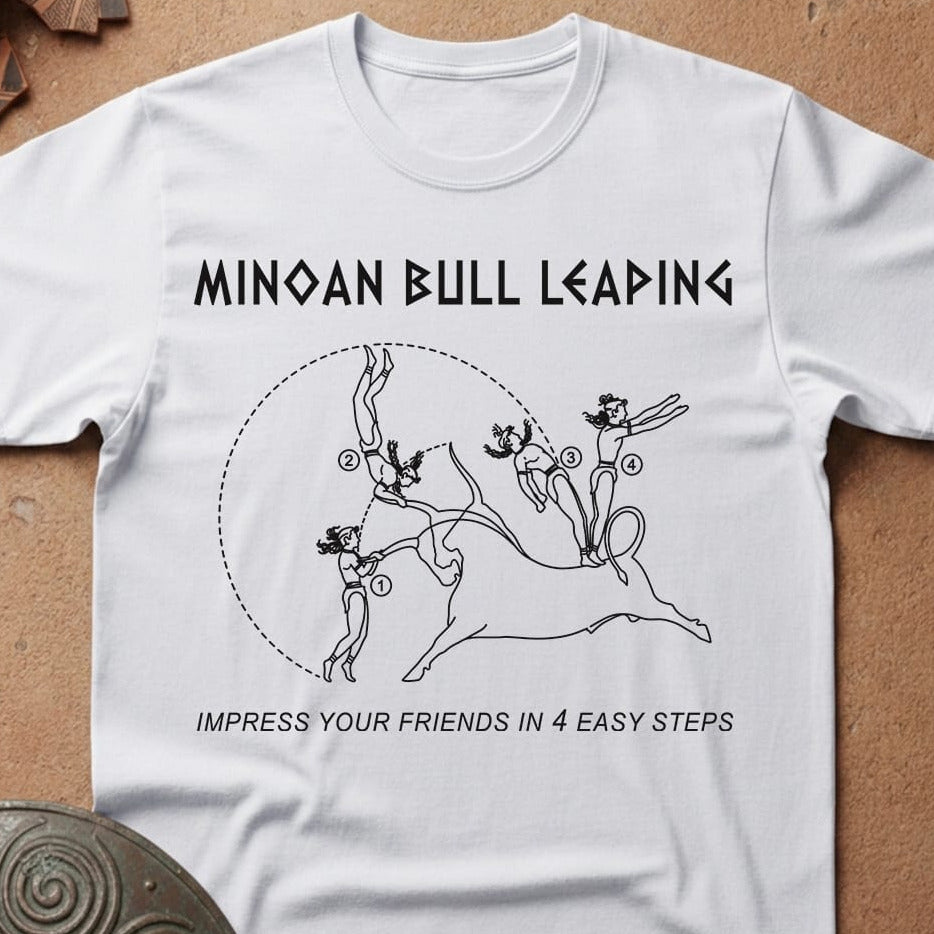 A white short-sleeve crewneck t-shirt laid flat on a textured brown surface. The shirt features a black graphic print of a Minoan bull with the text 'MINOAN BULL LEADING' above and 'IMPRESS YOUR FRIENDS IN 4 EASY STEPS' below.