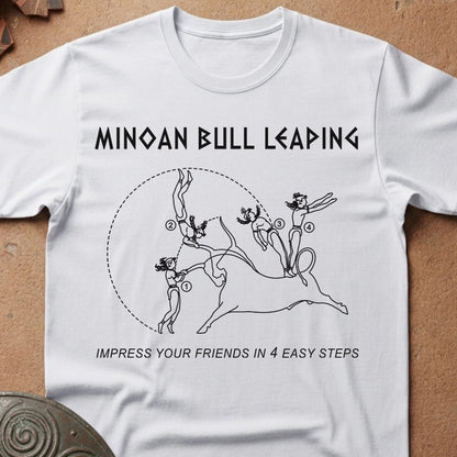 A white short-sleeve crewneck t-shirt laid flat on a textured brown surface. The shirt features a black graphic print of a Minoan bull with the text 'MINOAN BULL LEADING' above and 'IMPRESS YOUR FRIENDS IN 4 EASY STEPS' below.