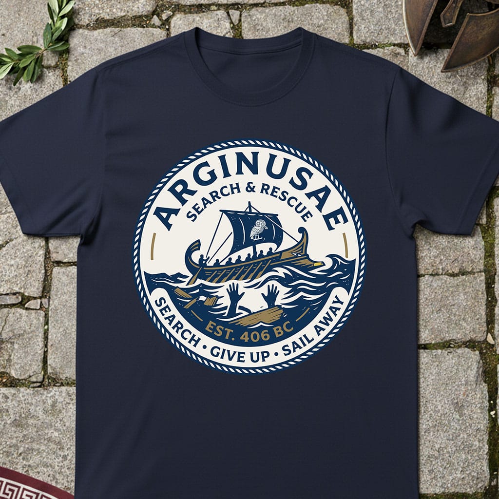 A navy blue crewneck t-shirt laid flat on a stone pavement background, featuring a large circular graphic print with a Viking ship, waves, and the text 'ARGINUSAE SEARCH & RESCUE'.