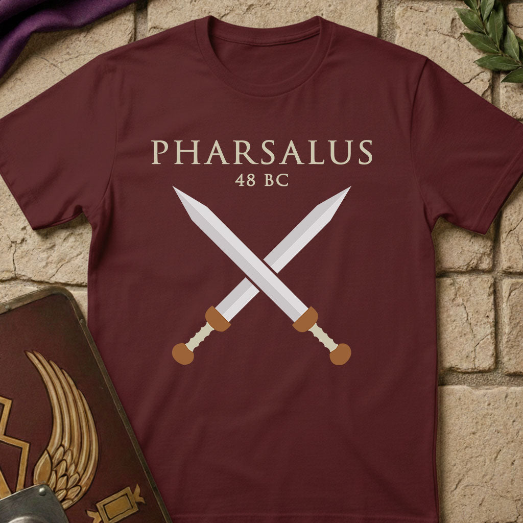 Maroon t-shirt with crossed swords and 'PHARSALUS 48 BC' text on a stone surface.
