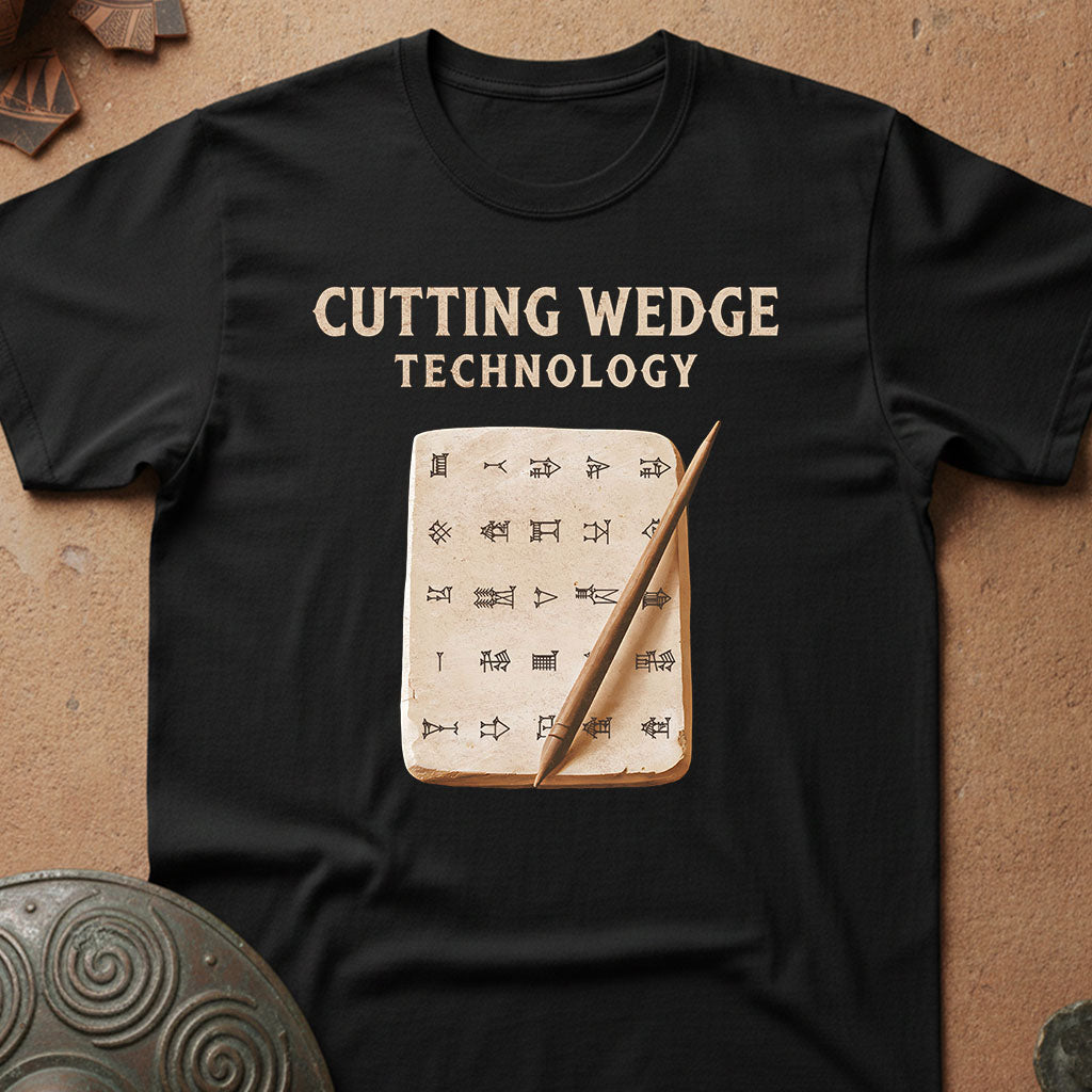 A black short-sleeve t-shirt laid flat on a textured brown surface, featuring the words 'CUTTING WEDGE TECHNOLOGY' in beige above a graphic of an open parchment with runic symbols and a wooden wedge.