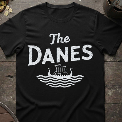 Black t-shirt with 'The Danes' and Viking ship design on a wooden surface.