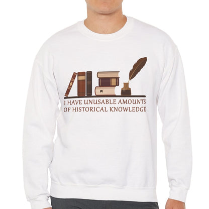 A man wearing a white crewneck sweatshirt with a brown graphic of books, an inkwell, and a quill, with the text 'I HAVE UNUSABLE AMOUNTS OF HISTORICAL KNOWLEDGE' printed on the front.
