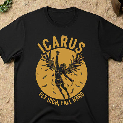 Black t-shirt with 'ICARUS FLY HIGH, FALL HARD' design on a sandy surface.