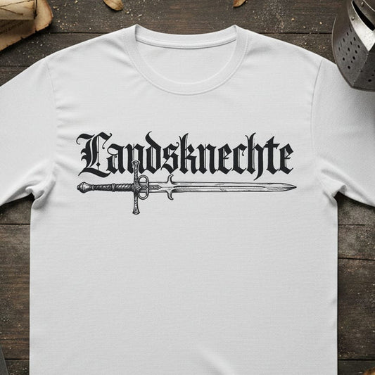 A white short-sleeve t-shirt laid flat on a rustic dark wood background, featuring a black gothic-style graphic that reads 'Landsknechte' above a detailed sword illustration.