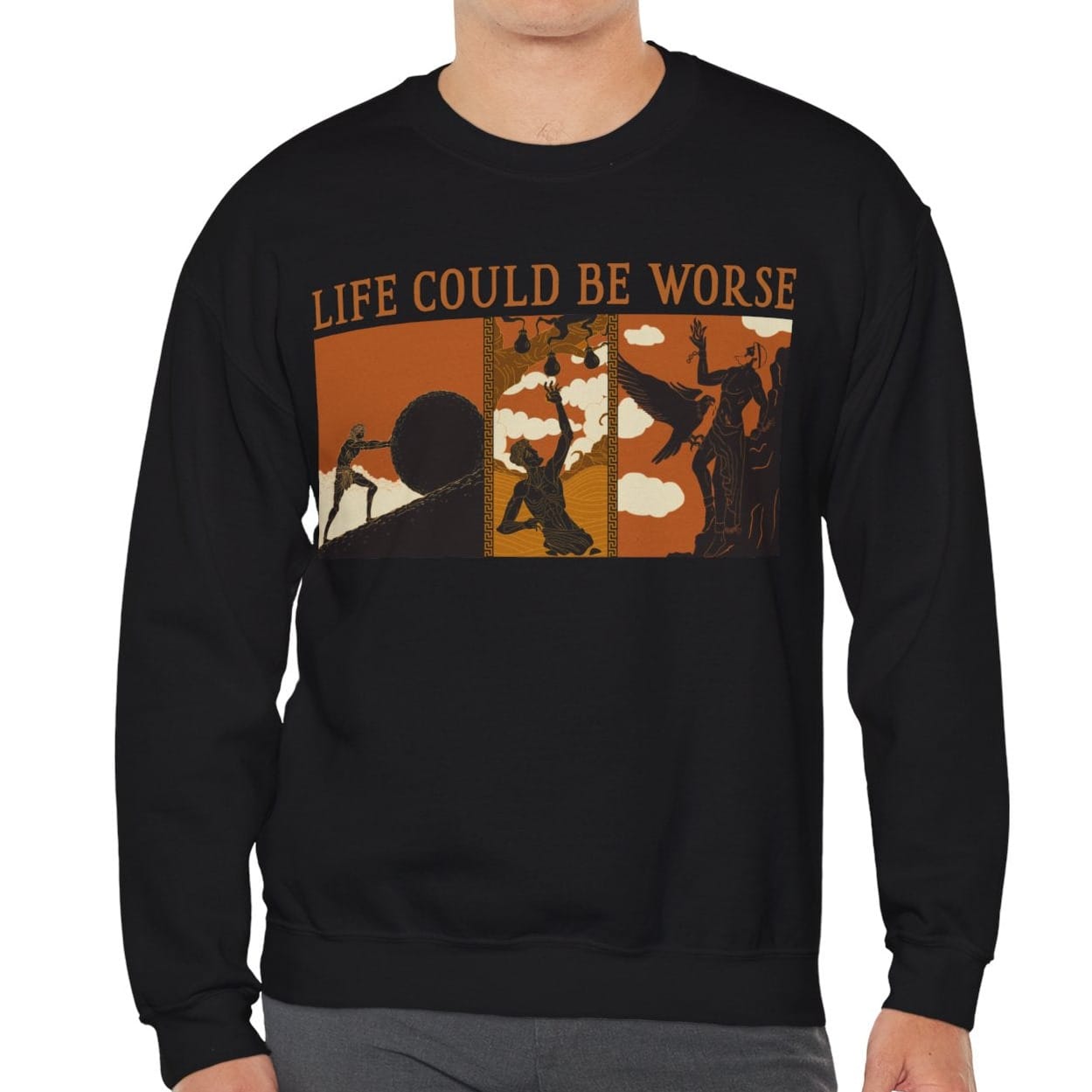 A man wearing a black crewneck sweatshirt with a graphic print that reads 'LIFE COULD BE WORSE' above an abstract orange, brown, and black illustration, paired with gray pants, against a plain white background.
