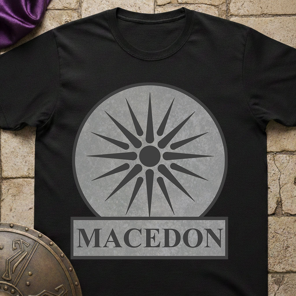 Black t-shirt with a gray sun-like symbol and 'Macedon' text on a stone surface.