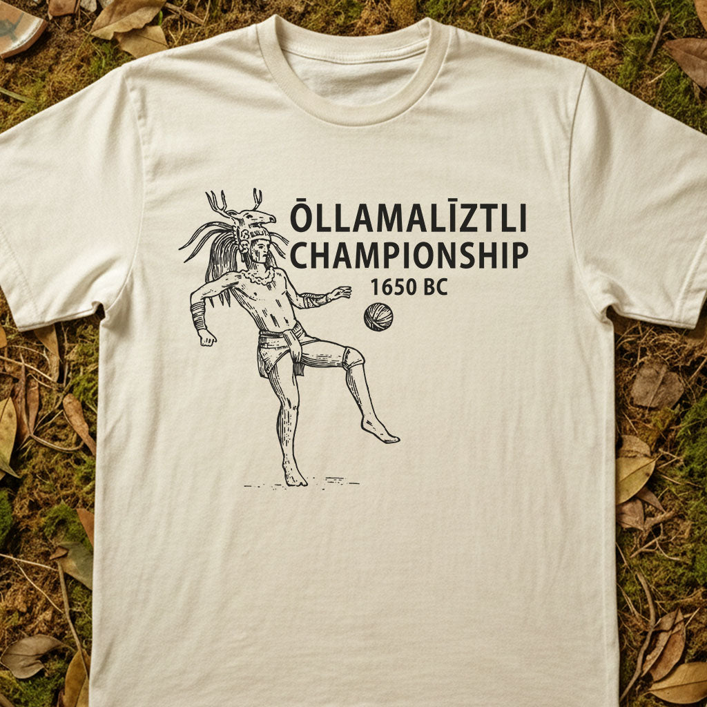 White t-shirt with a graphic design of a person playing a ball game and text 'Ollamaliztli Championship 1650 BC' on grass.