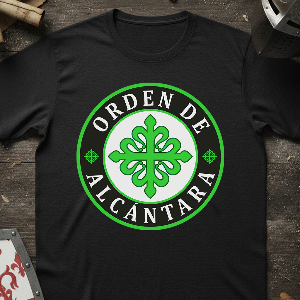 A black short-sleeve t-shirt laid flat on a dark rustic wooden surface, featuring a large circular green and white graphic on the chest that reads 'ORDEN DE ALCANTARA' around a green ornamental emblem.