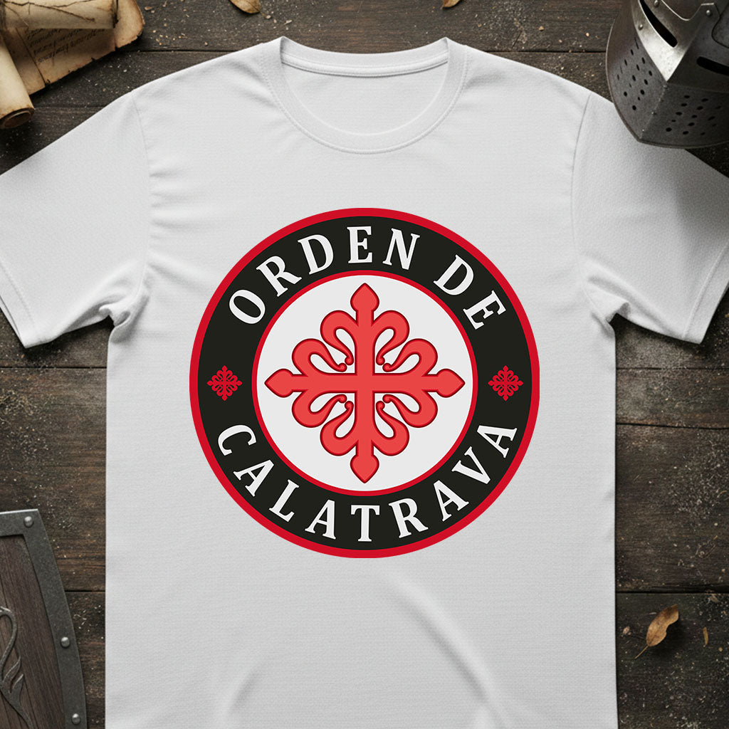 A white short-sleeve t-shirt laid flat on a dark rustic wooden surface, featuring a circular graphic print with the text 'ORDEN DE CALATRAVA' in white on a black ring and a red ornamental emblem in the center.
