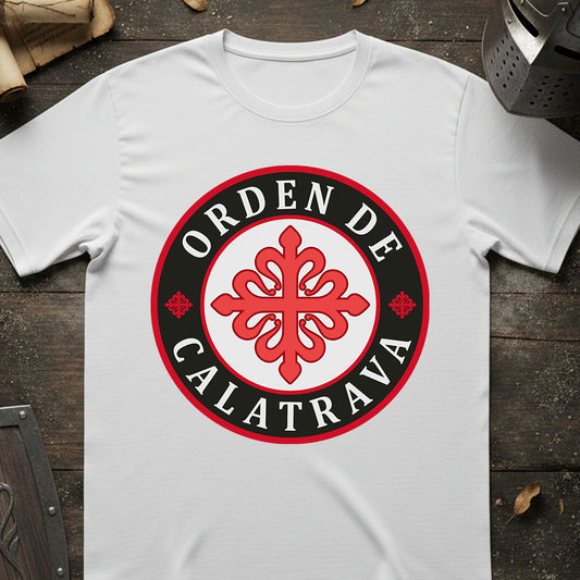 A white short-sleeve t-shirt laid flat on a dark rustic wooden surface, featuring a circular graphic print with the text 'ORDEN DE CALATRAVA' in white on a black ring and a red ornamental emblem in the center.