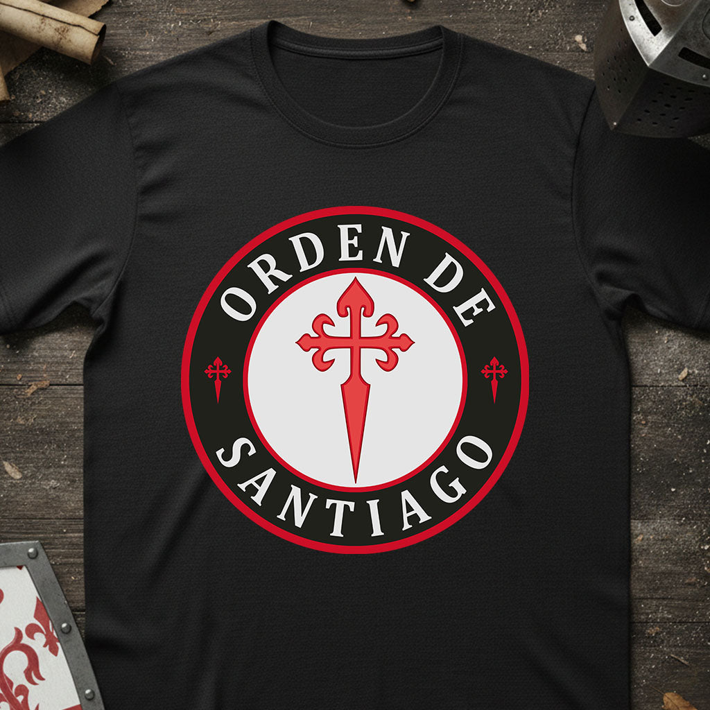 A black short-sleeve t-shirt laid flat on a rustic dark wood surface, featuring a large circular graphic on the chest with the words 'ORDEN DE SANTIAGO' in white around a red and white central emblem.