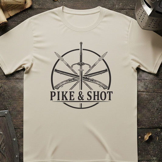 A cream-colored short-sleeve t-shirt with a black graphic print of crossed weapons and the text 'PIKE & SHOT' laid flat on a dark rustic wooden surface.