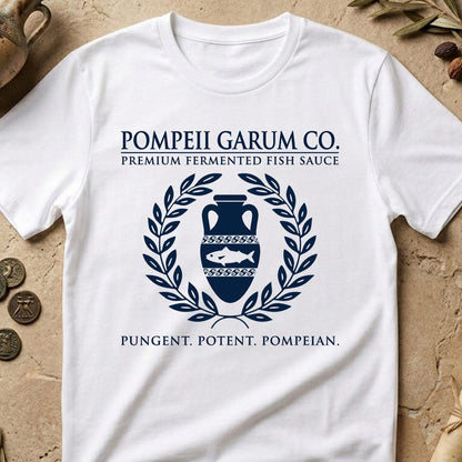 A white short-sleeve graphic T-shirt laid flat on a textured beige stone surface. The shirt features a dark navy blue printed design reading 'POMPEII GARUM CO.