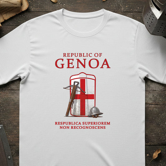 A white short-sleeve T-shirt laid flat on a dark wooden surface, featuring a red and white Genoa graphic with the words 'REPUBLIC OF GENOA' and a historical flag design. Decorative props including a helmet, scroll, and shield are partially visible around the edges.