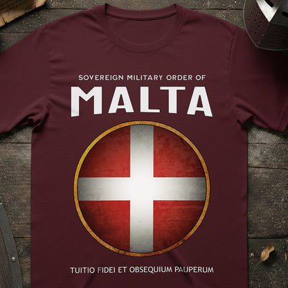 Maroon t-shirt with Sovereign Military Order of Malta logo on a wooden surface