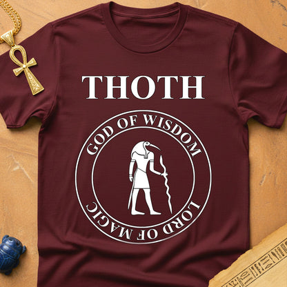 Maroon t-shirt with 'THOTH, God of Wisdom, Lord of Magic' design on a wooden surface.