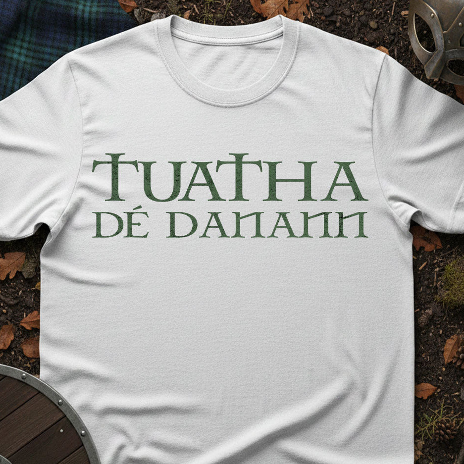 White t-shirt with green text 'TUATHA Üd Danann' on a natural background