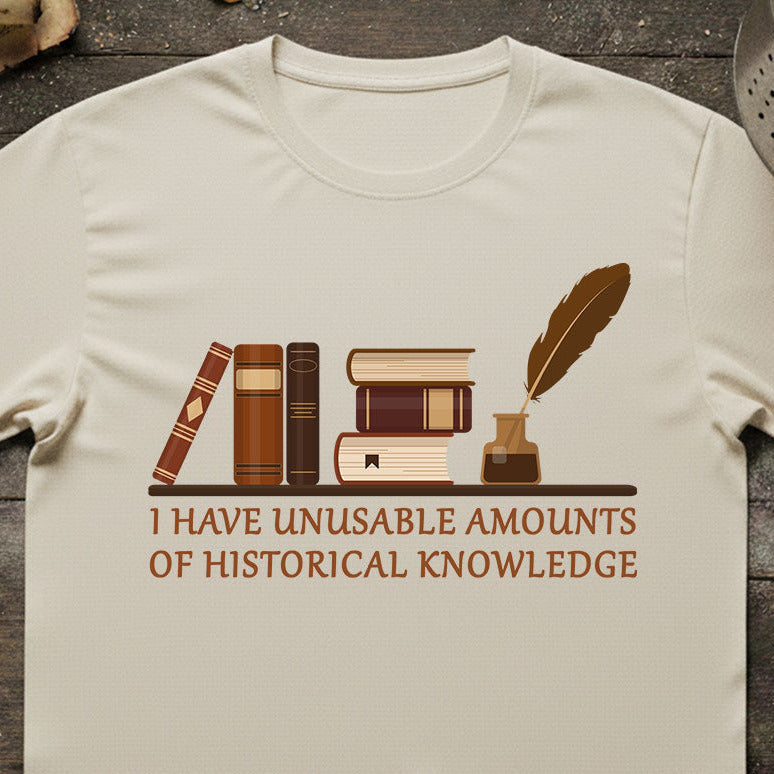 Beige t-shirt with books and quill design and text on a wooden surface