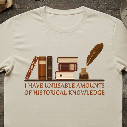 Beige t-shirt with books and quill design and text on a wooden surface