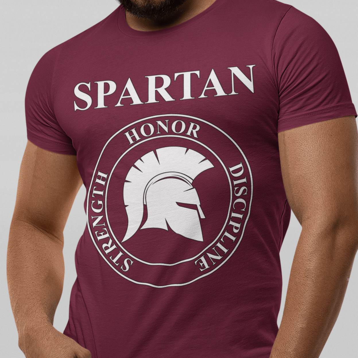 A man wearing a maroon short-sleeve t-shirt with a white graphic print that reads 'SPARTAN' above a circular emblem featuring a Spartan helmet and the words 'HONOR', 'STRENGTH', 'DISCIPLINE'.