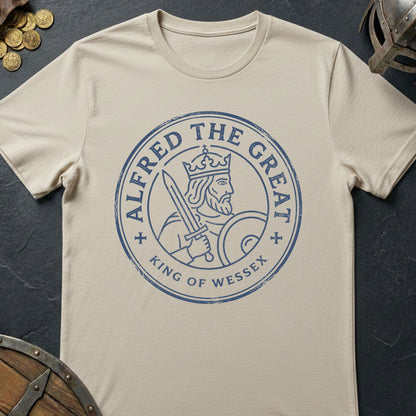 Beige t-shirt with 'Alfred the Great, King of Wessex' design on a dark surface with coins and a helmet.